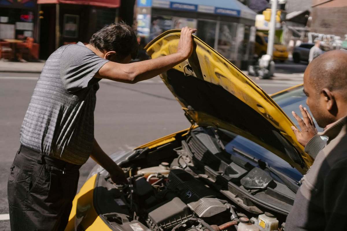 Deux hommes examinent le moteur d'une voiture jaune sur une rue