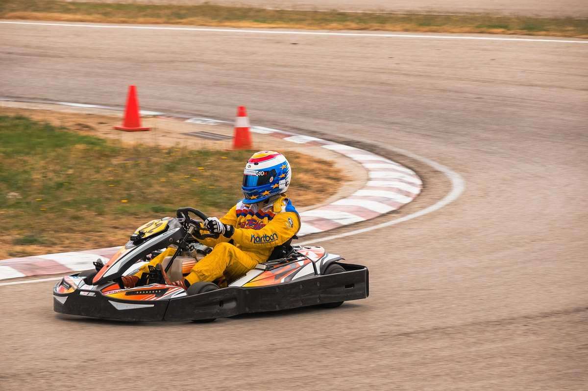 Pilote de kart en virage sur circuit, cônes de sécurité orange Pilote de kart en virage sur circuit, cônes de sécurité orange