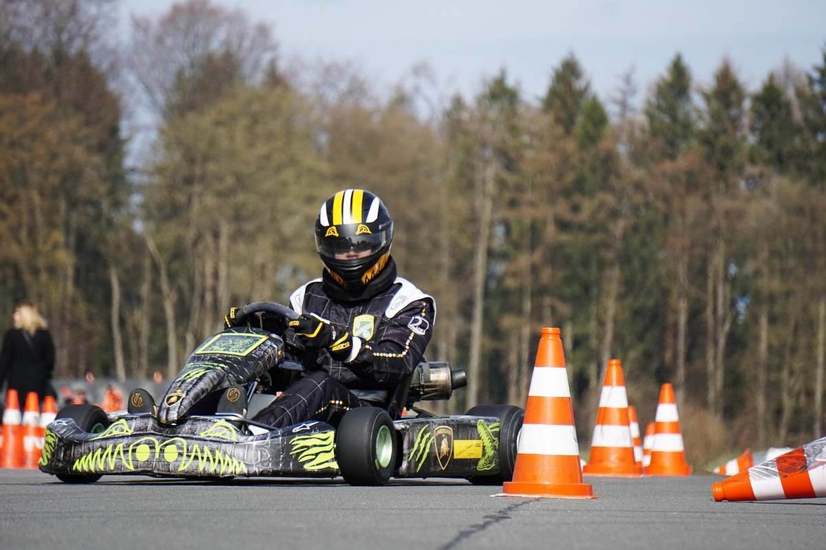 Pilote de kart en combinaison noire et jaune pilotant dans un virage, cônes oranges visibles en arrière-plan