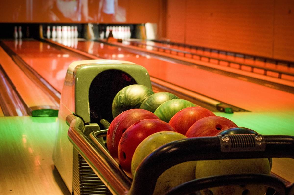 Bowling, balles colorées dans le porte-balles, pistes et quilles visibles