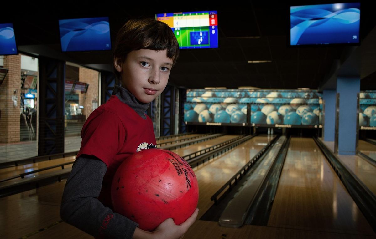 Un jeune garçon tient une boule rouge près d'une voie de bowling