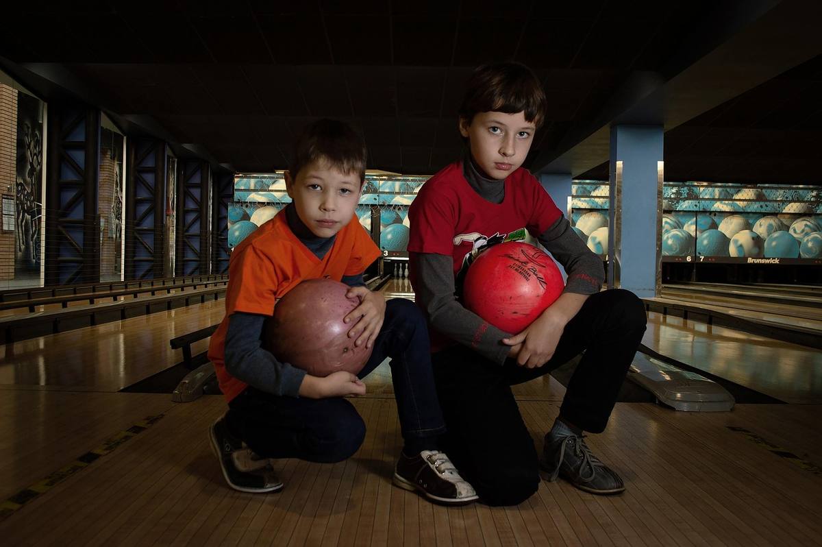 Deux enfants crouchés dans une allée de bowling, tenant leurs boules