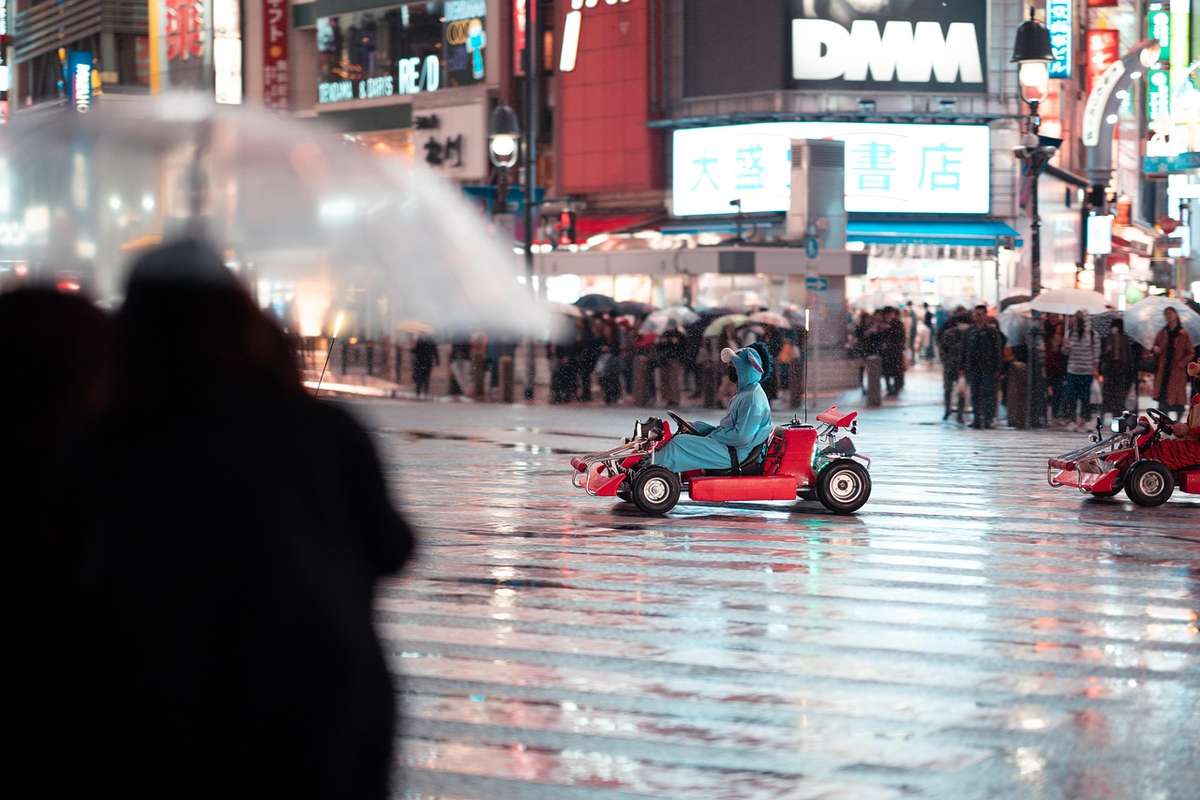 Une personne conduit une petite voiture rouge sur une rue mouillée, foule sous parapluies