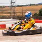 Pilote vêtu d'une combinaison jaune conduisant un kart sur une piste avec barrières rouges et blanches