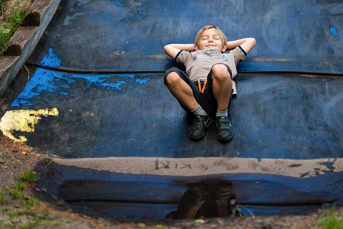 Enfant allongé sur une surface bleue, bras derrière la tête, en position de relaxation
