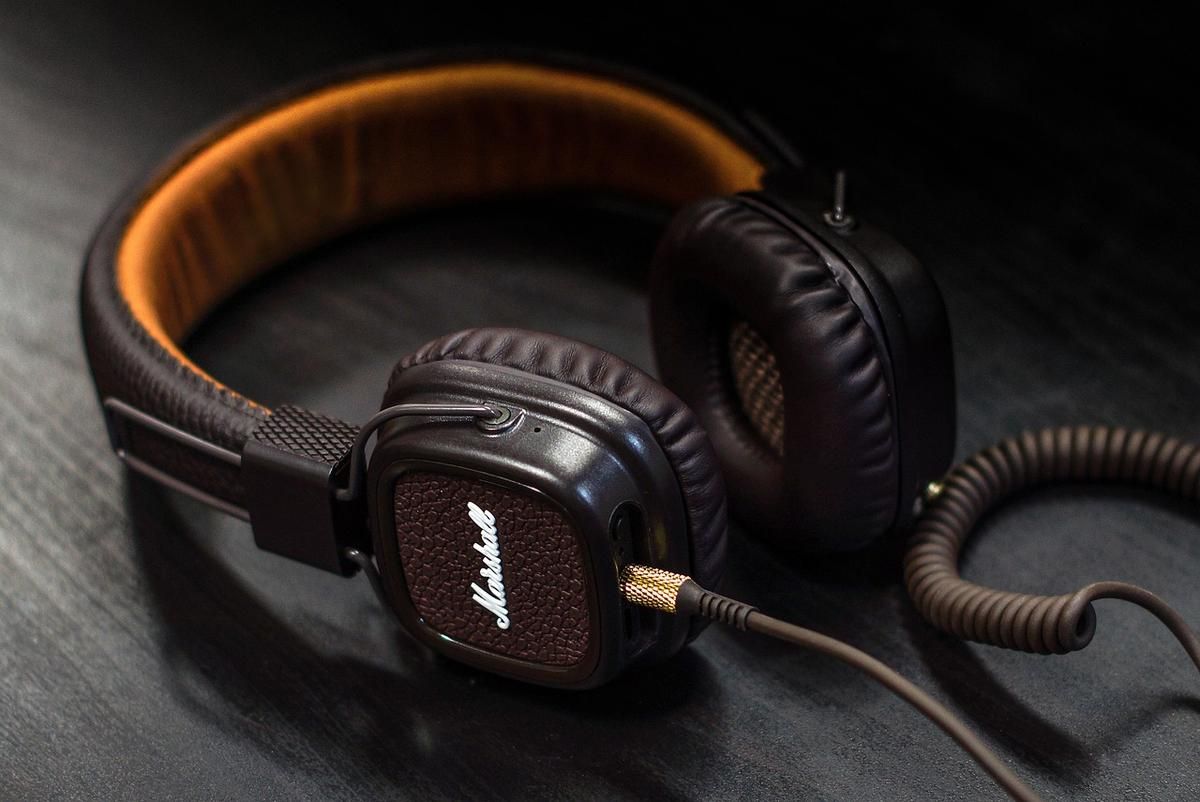 Casque Marshall noir et orange sur fond sombre avec câble enroulé