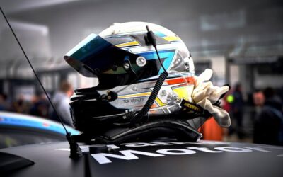 Un casque de course posé sur une voiture, gantée, stand de pit